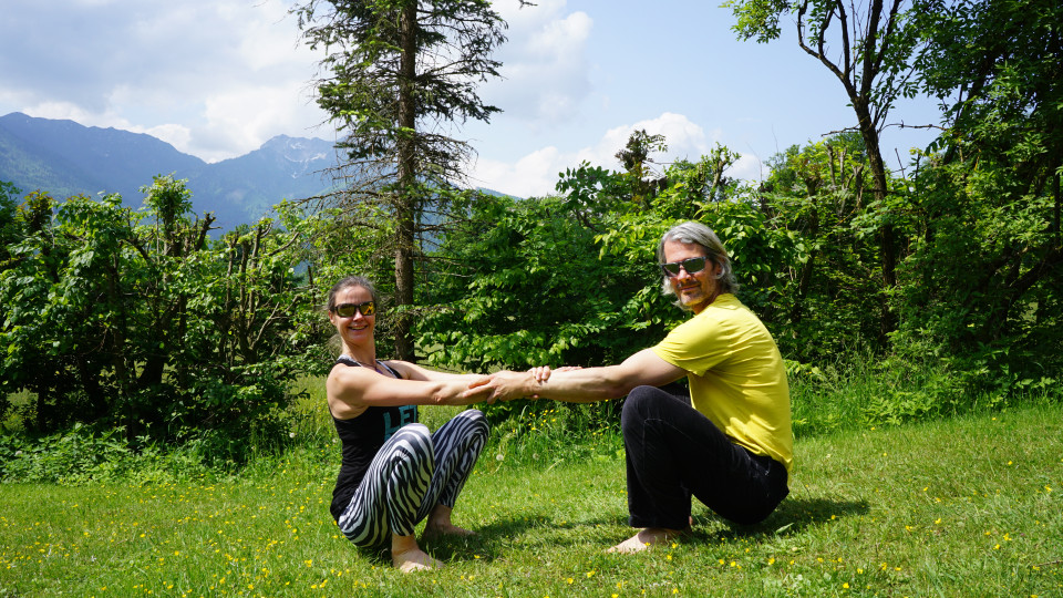 Die Partner kommen gegenüber voneinander in ein Malasana, greifen sich an den Unterarmen und verlagern das Gewicht voneinander weg. Entweder bleiben oder gemeinsam hoch und tief gehen. 